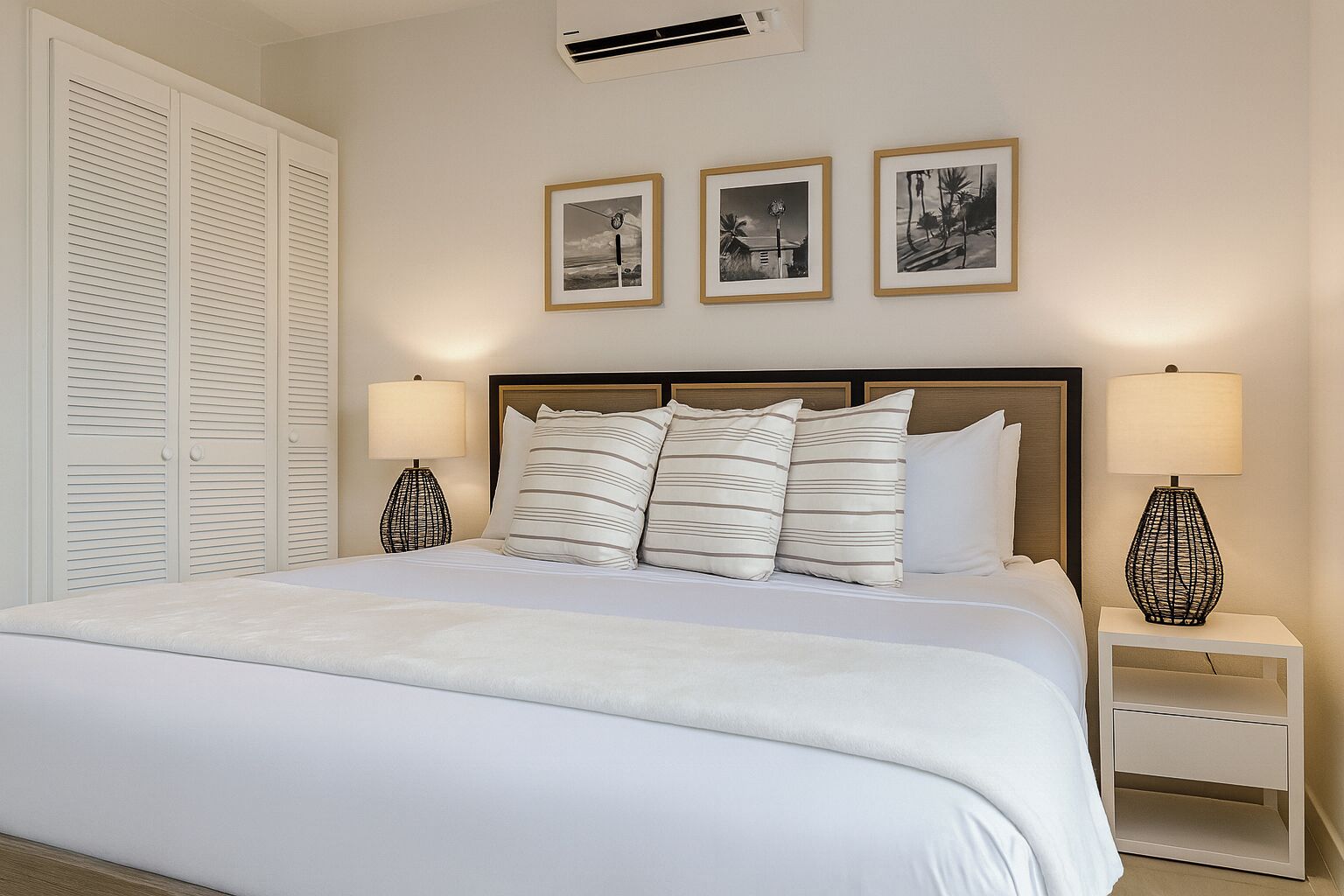 Una cama bien hecha con almohadas a rayas, dos mesitas de noche con lámparas y tres cuadros en la pared.