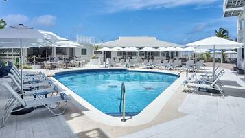 Una piscina al aire libre, sombrillas, sillones reclinables de piscina