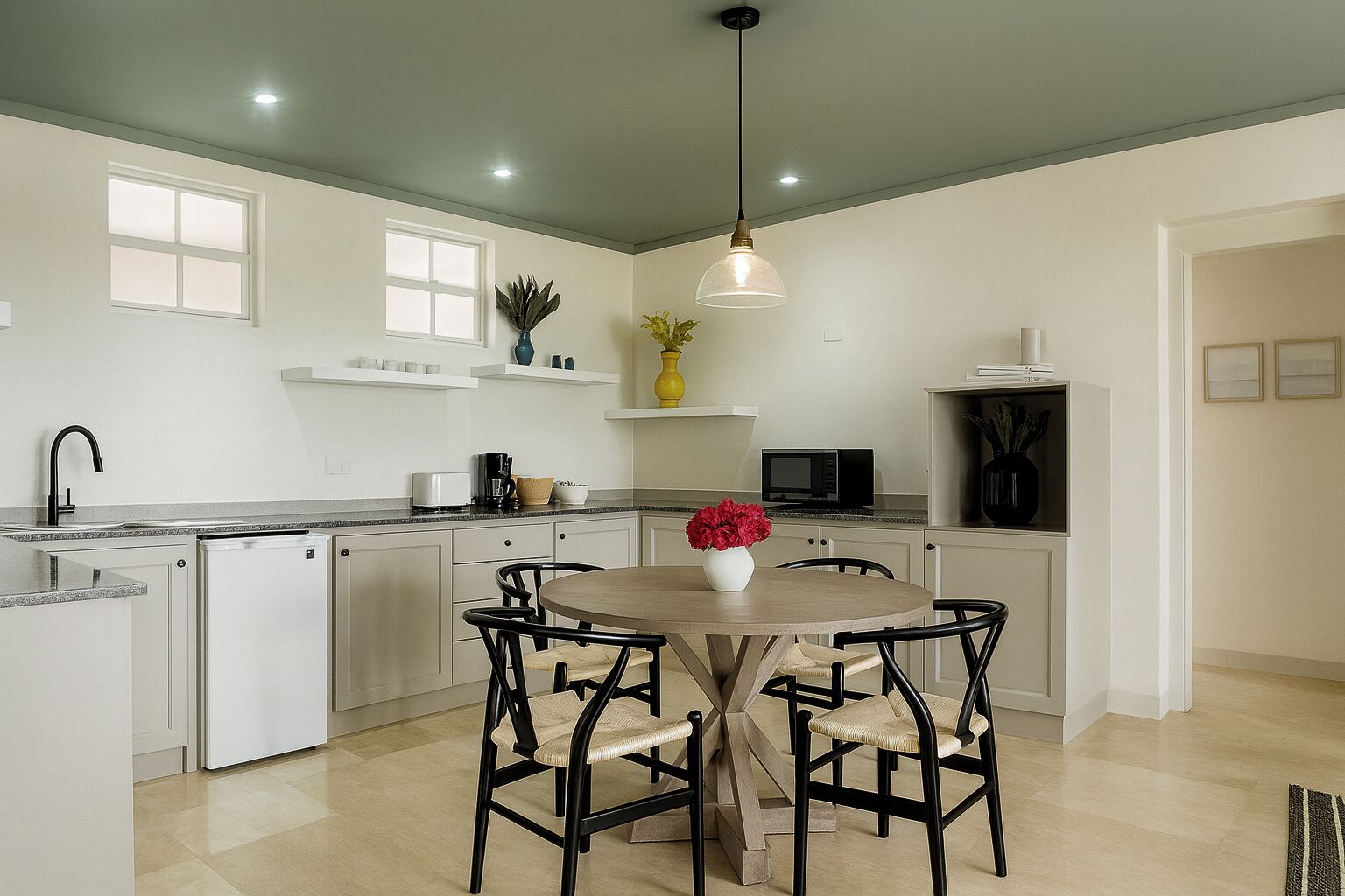 A modern kitchen with white cabinetry, a round dining table with four chairs, a hanging light fixture, and a microwave on the countertop.