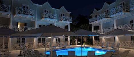 A poolside area with lounge chairs and umbrellas, surrounded by multi-story buildings with balconies.