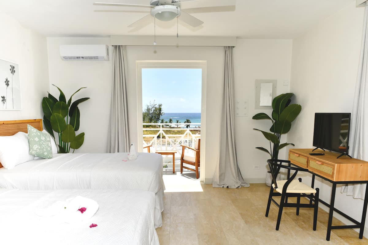 A hotel room with a bed, a desk, a chair, a television, and a balcony with a view of the ocean.