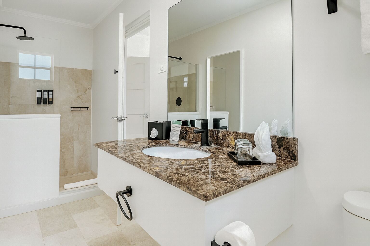 A modern bathroom with a marble countertop, a white sink, a large mirror, and a shower area.