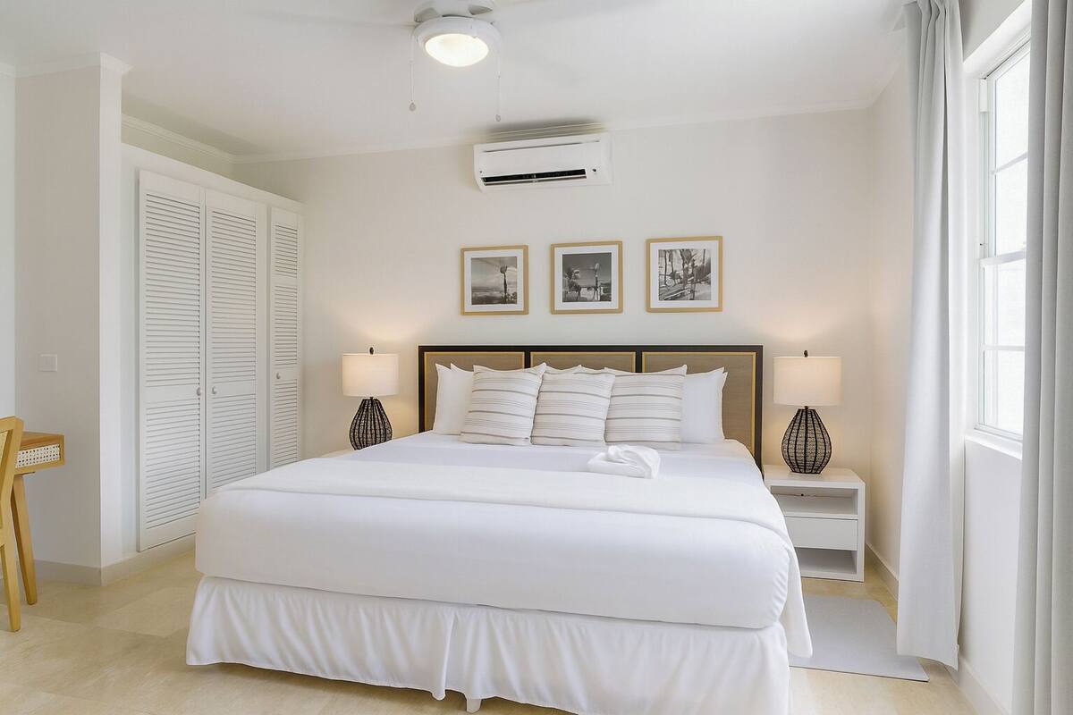 A neatly arranged bedroom with a large bed, two bedside tables with lamps, a wardrobe, and framed pictures on the wall.