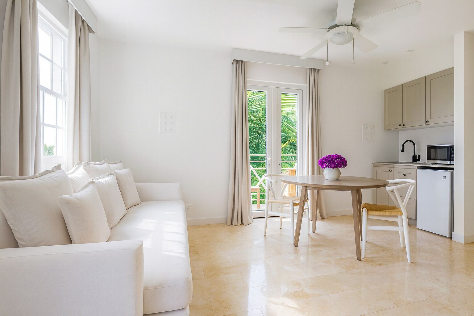 Una sala de estar moderna con un sofá blanco, una mesa de comedor con sillas, una zona de cocina con armarios y electrodomésticos, y un balcón con cortinas.