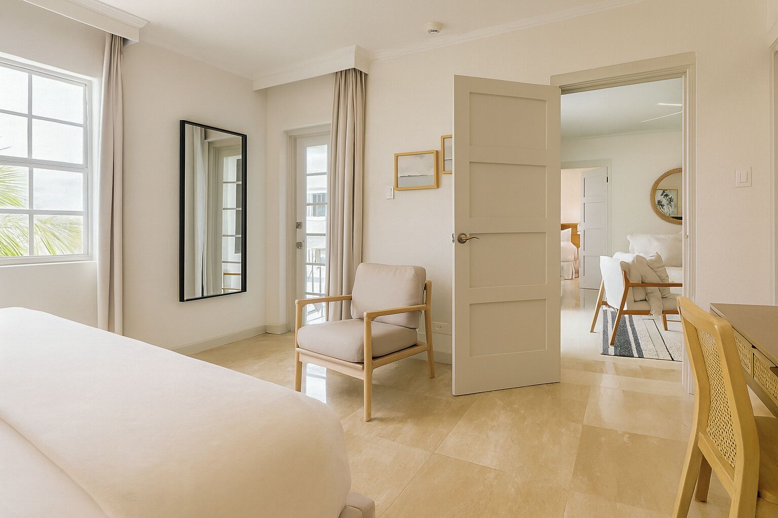 A hotel room with a bed, a chair, a desk, and a door leading to another room.