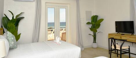 A hotel room with two beds, a television, a desk, and large windows with a view of the sea.