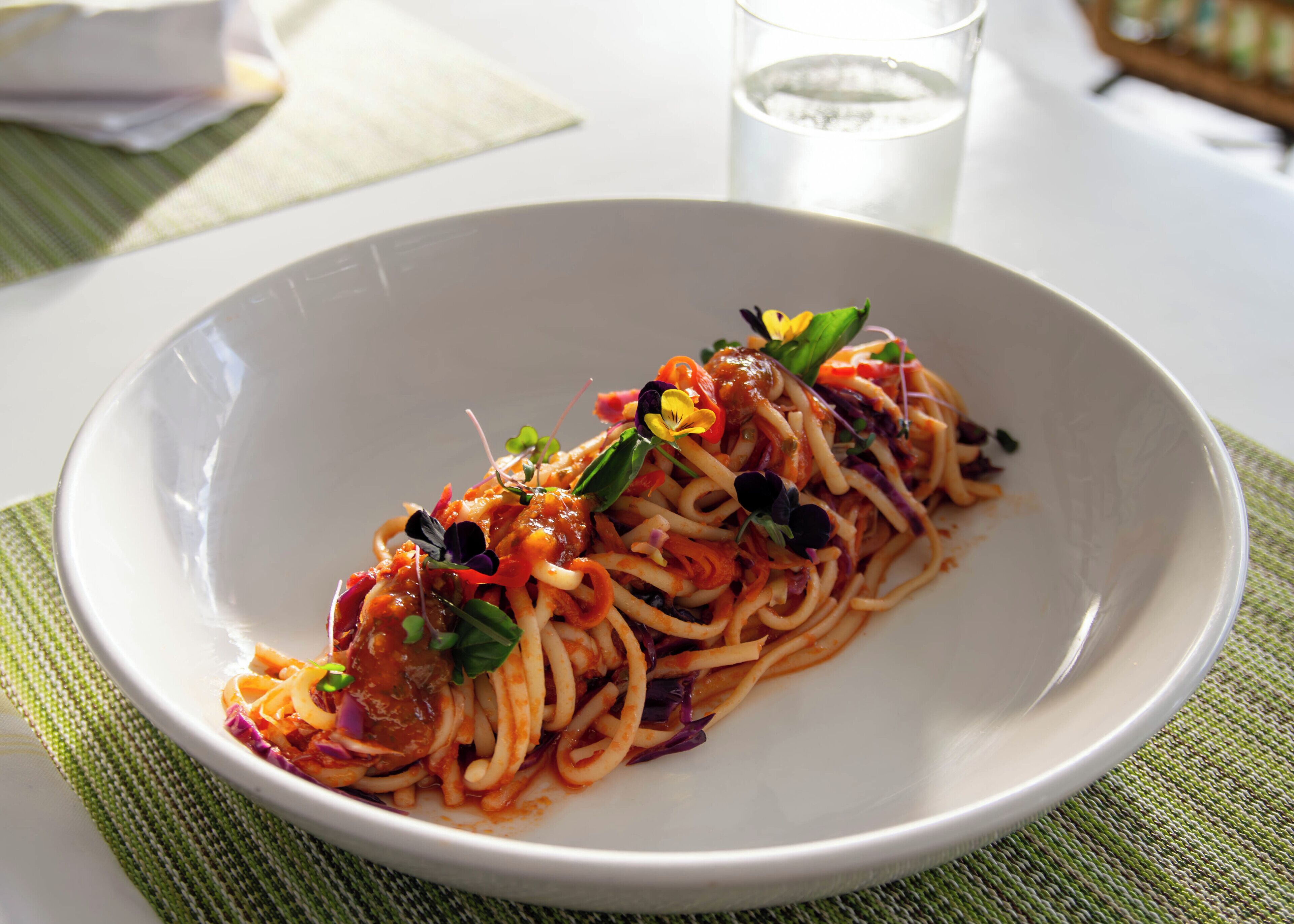 A plate of spaghetti with vegetables and herbs.