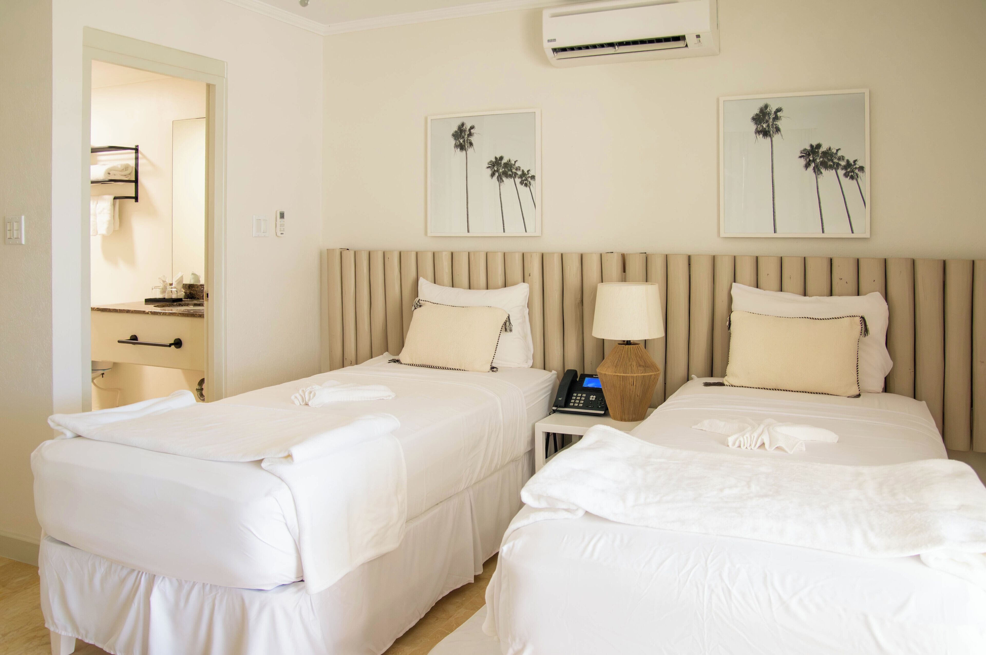 A hotel room with two beds, a bedside table with a lamp, and a mirror.