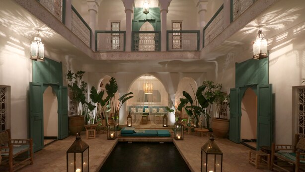 A luxurious indoor pool area with a central seating area, surrounded by potted plants and wooden furniture. - Riad DAR DAR (Marrakech)
