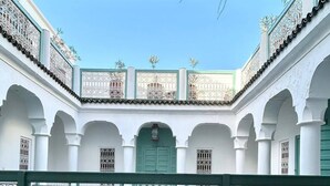 A dining table set with breakfast items, including bread, eggs, and fruit, in a courtyard with white arches and decorative metal railings. - Riad DAR DAR (Marrakech)