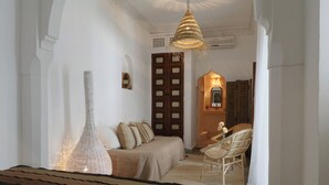 A room with a bed, a large vase, a hanging light fixture, a wooden door, and a chair. - Riad DAR DAR (Marrakech)