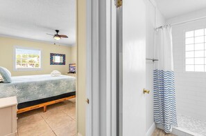 A bedroom with a bed, a window, a ceiling fan, and a bathroom with a shower curtain. - TROUT Steps to beach. Lovely two bedroom with screened porch and pool. (St. George Island)