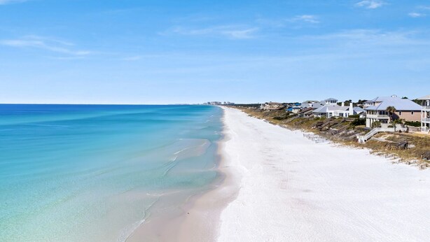 A coastal beach with white sand, clear turquoise water, and houses with balconies overlooking the ocean. - Sea Blue Escape | 30A 2BR | Pool + Walk to Beach (Santa Rosa Beach)