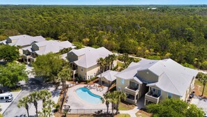 A residential area with multiple houses, a swimming pool, and a forested background. - Sea Blue Escape | 30A 2BR | Pool + Walk to Beach (Santa Rosa Beach)