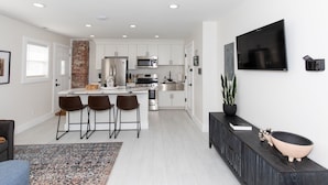 A modern kitchen with white cabinets, stainless steel appliances, and a central island with bar stools. - Inn at Fulton: Unit 5 (Sandusky)