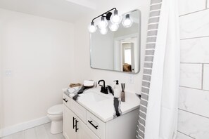 Een moderne badkamer met een witte wastafel, een zwarte kraan en een spiegel erboven. Een handdoekhouder en een toilet zijn zichtbaar.