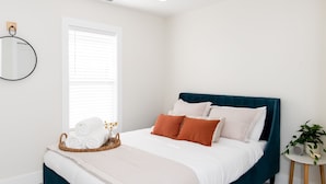 Quarto com cama, mesa de cabeceira, janela e espelho fixado na parede.