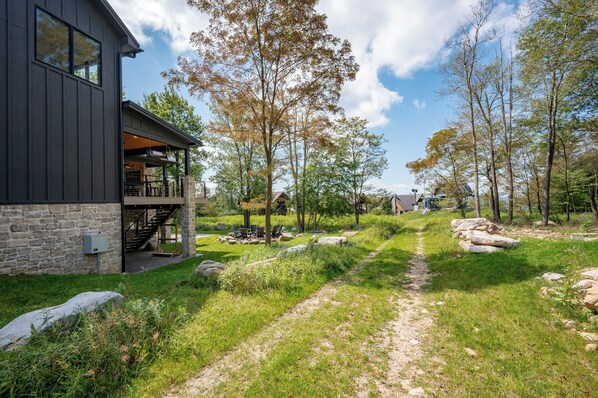 Et moderne hus med en stenfacade, et overdækket udeområde og en grusvej, der fører gennem et skovområde.