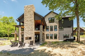 A two-story stone house with a large chimney, outdoor seating, and a grill area.