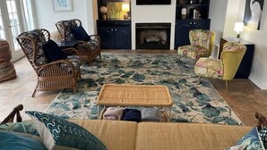 A living room with wicker furniture, a large floral rug, and a flat-screen TV mounted on the wall. - BEAUTIFUL LAKE HAMILTON COTTAGE - GREAT LOCATION, GREAT VIEWS - ADORABLE  3BD/3B (Hot Springs)