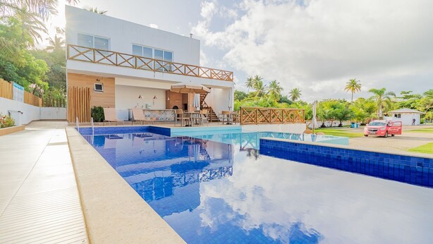 A modern hotel with a large outdoor swimming pool, a covered seating area, and a view of the surrounding greenery. - IM05 Apto 3 Quartos - Riverside Imbassaí (Mata de São João)