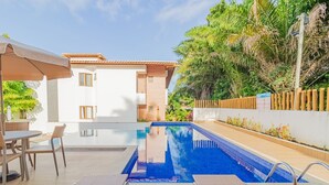 Una piscina con sillones de descanso, un espacio de estar techado y un edificio con tejado de baldosas.