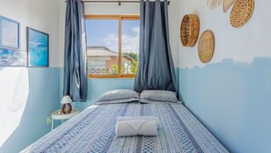 Un dormitorio con cama, cortinas, mesita de noche, lámpara y adornos en la pared.