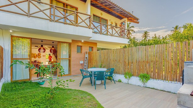 Un edificio de dos pisos con un balcón, una cerca de madera y un patio con mesa y sillas.
