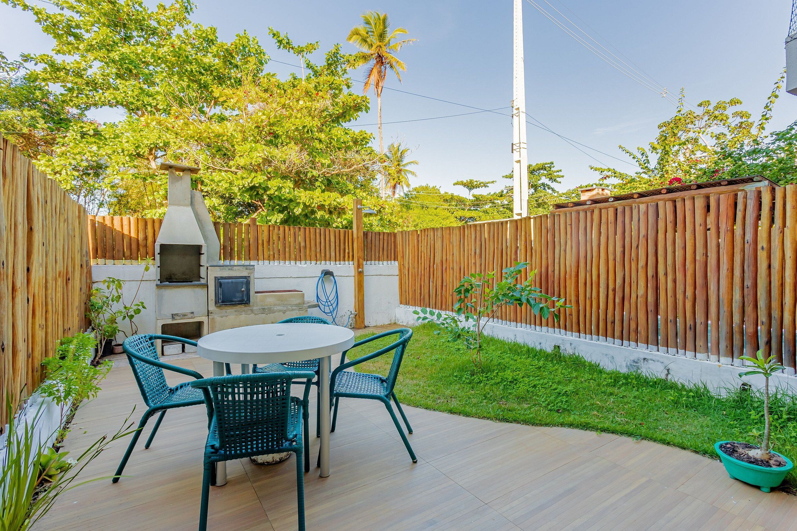 Une terrasse extérieure avec une table ronde et quatre chaises, entourée d’une clôture en bois et de verdure.