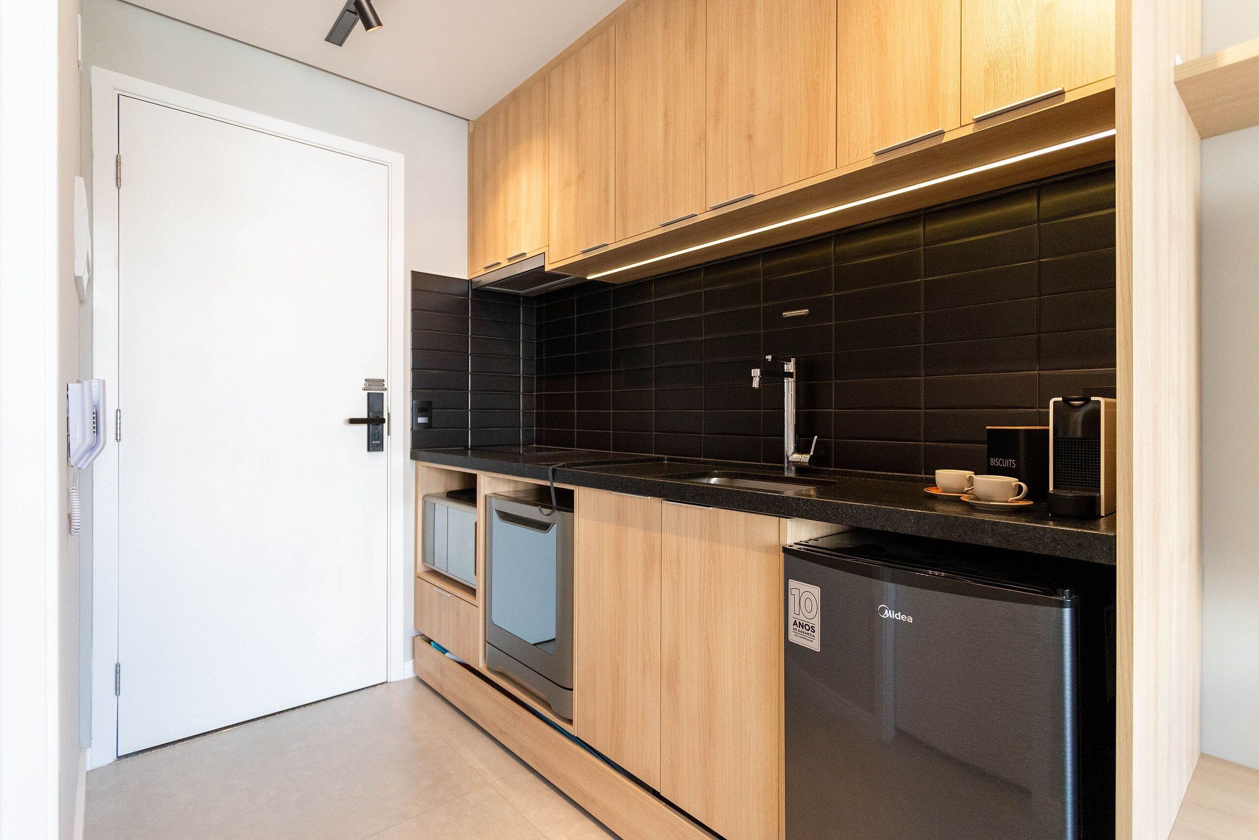 A modern kitchen with wooden cabinets, black countertops, a built-in dishwasher, and a refrigerator.