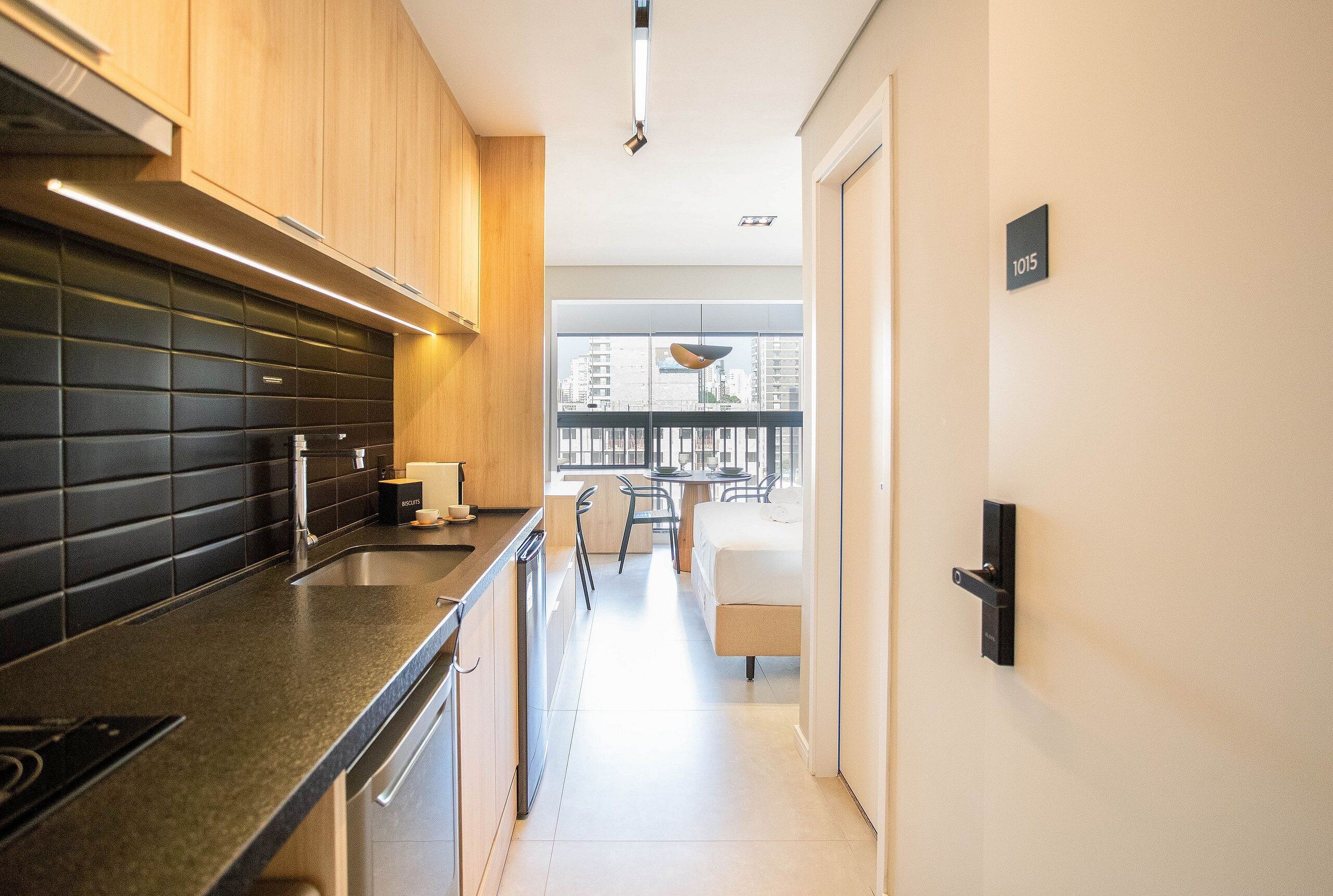 Een moderne keuken met zwarte tegels, houten kastjes en een eethoek met uitzicht op gebouwen.