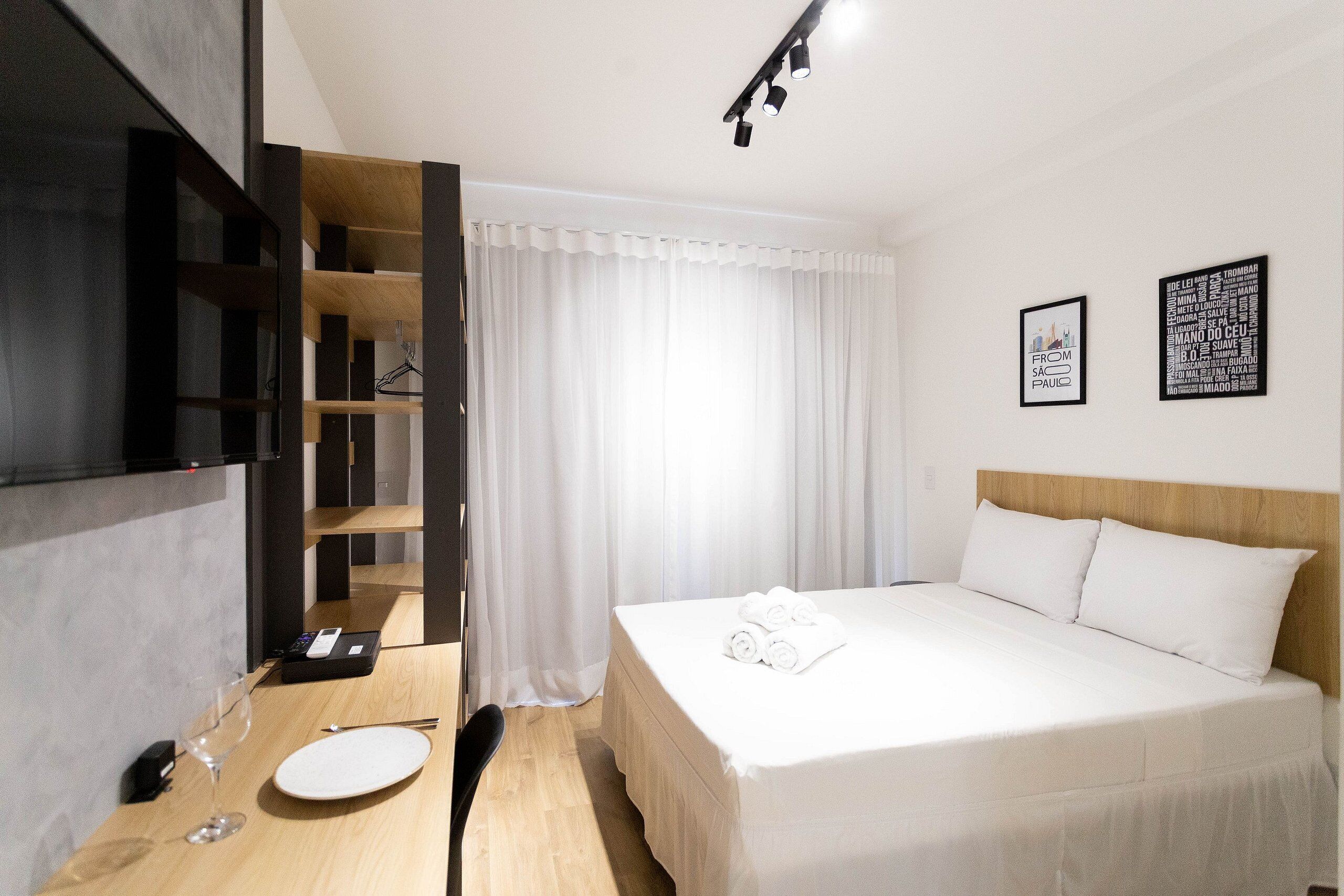 Habitación de hotel con cama, escritorio, silla, televisor y dos cuadros en la pared.