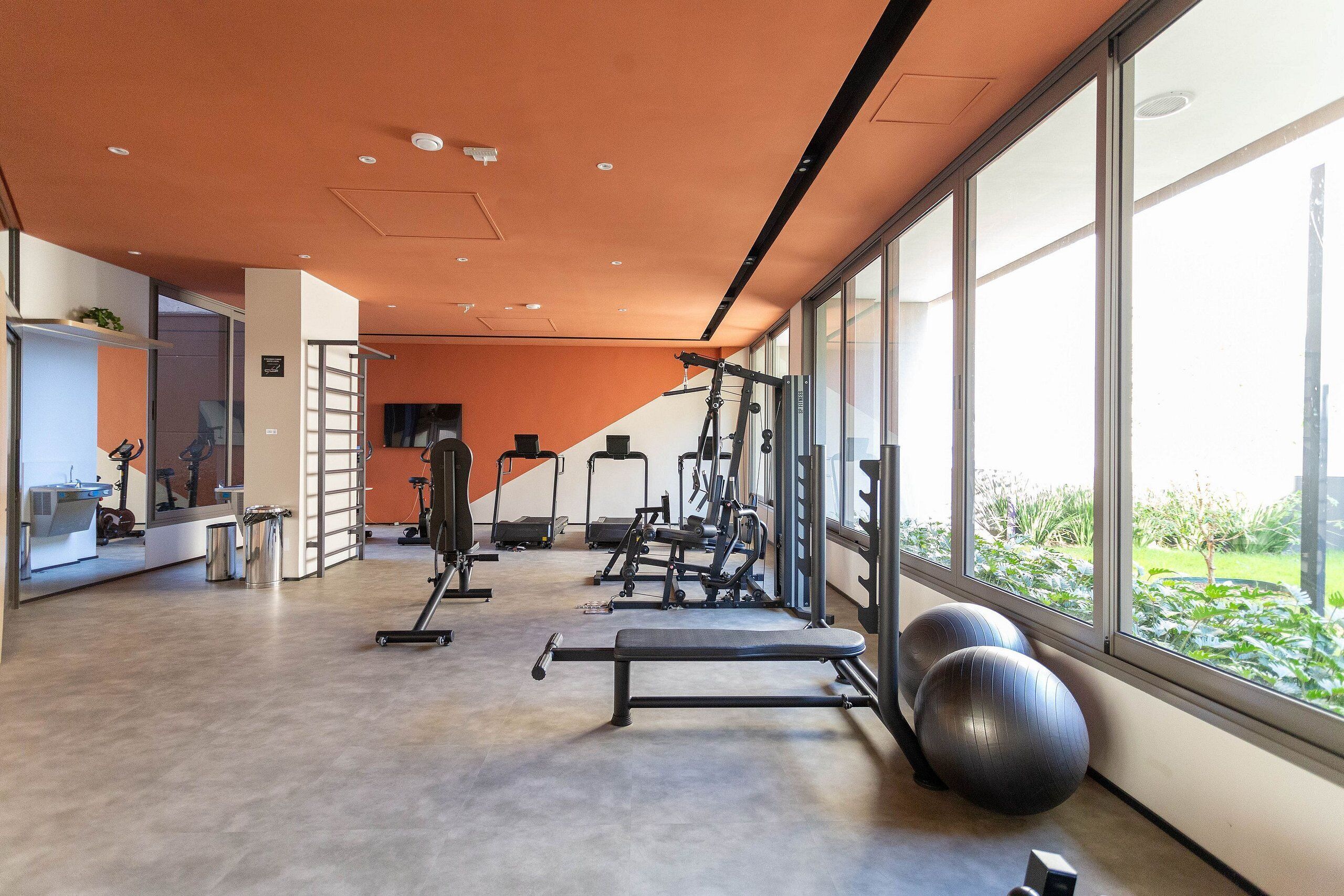 Une salle de sport moderne, équipée de matériel d’exercice, dotée de grandes fenêtres et offrant une vue sur la verdure environnante.