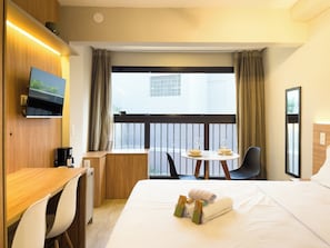 A hotel room with a bed, a desk, a chair, a small table with glasses, and a TV on the wall. - Nik Perdizes (São Paulo)