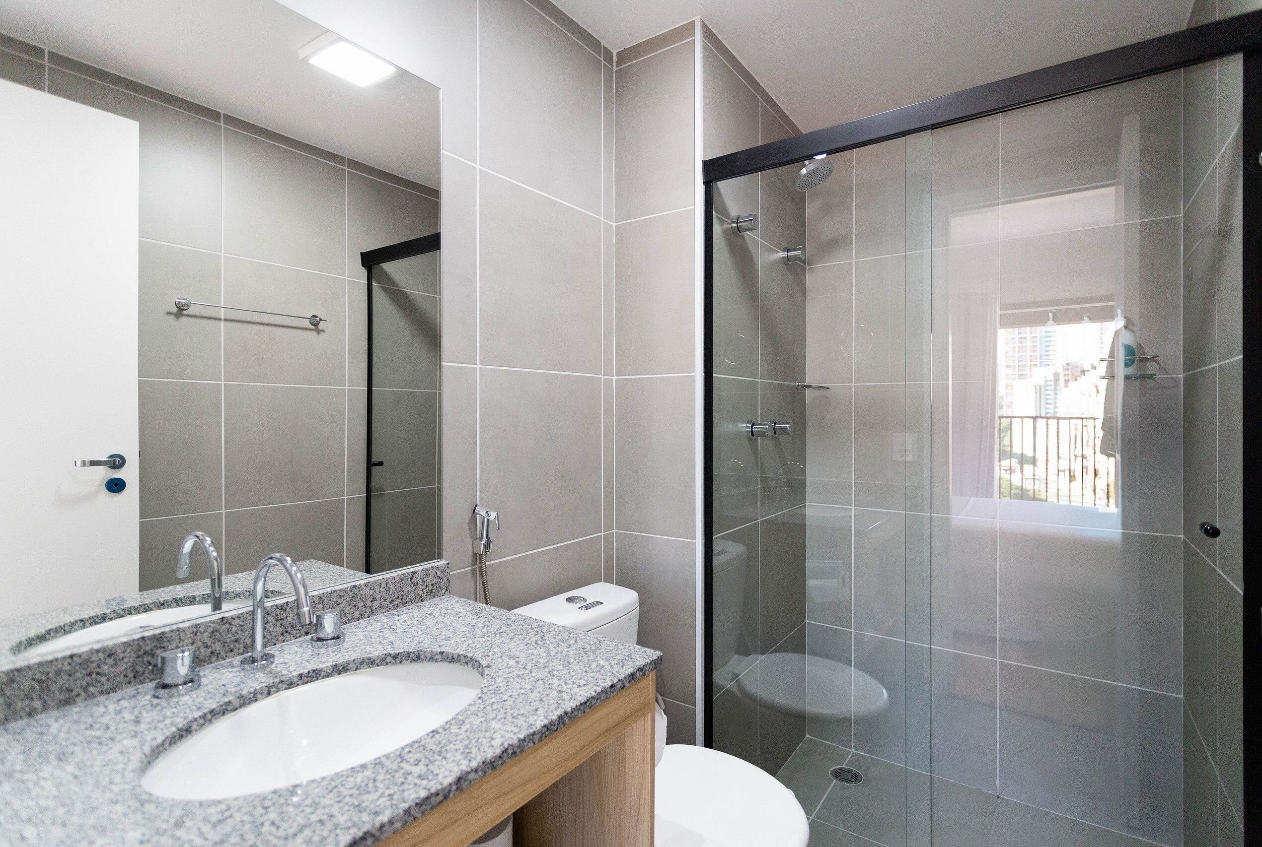 A modern bathroom with a granite countertop sink, a mirror, and a glass-enclosed shower.
