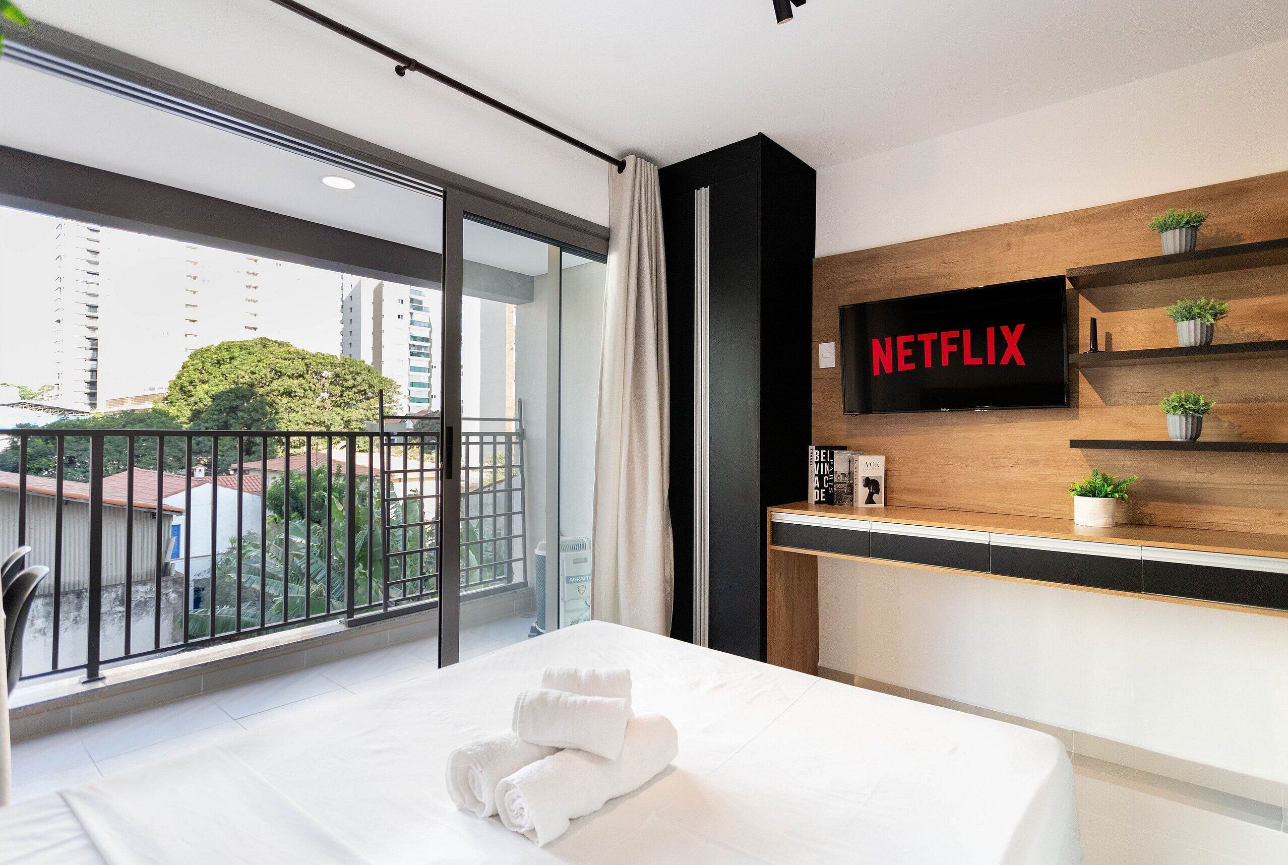 Habitació d'hotel moderna amb un llit gran, un televisor fixat a la paret i un balcó amb vistes a la ciutat.