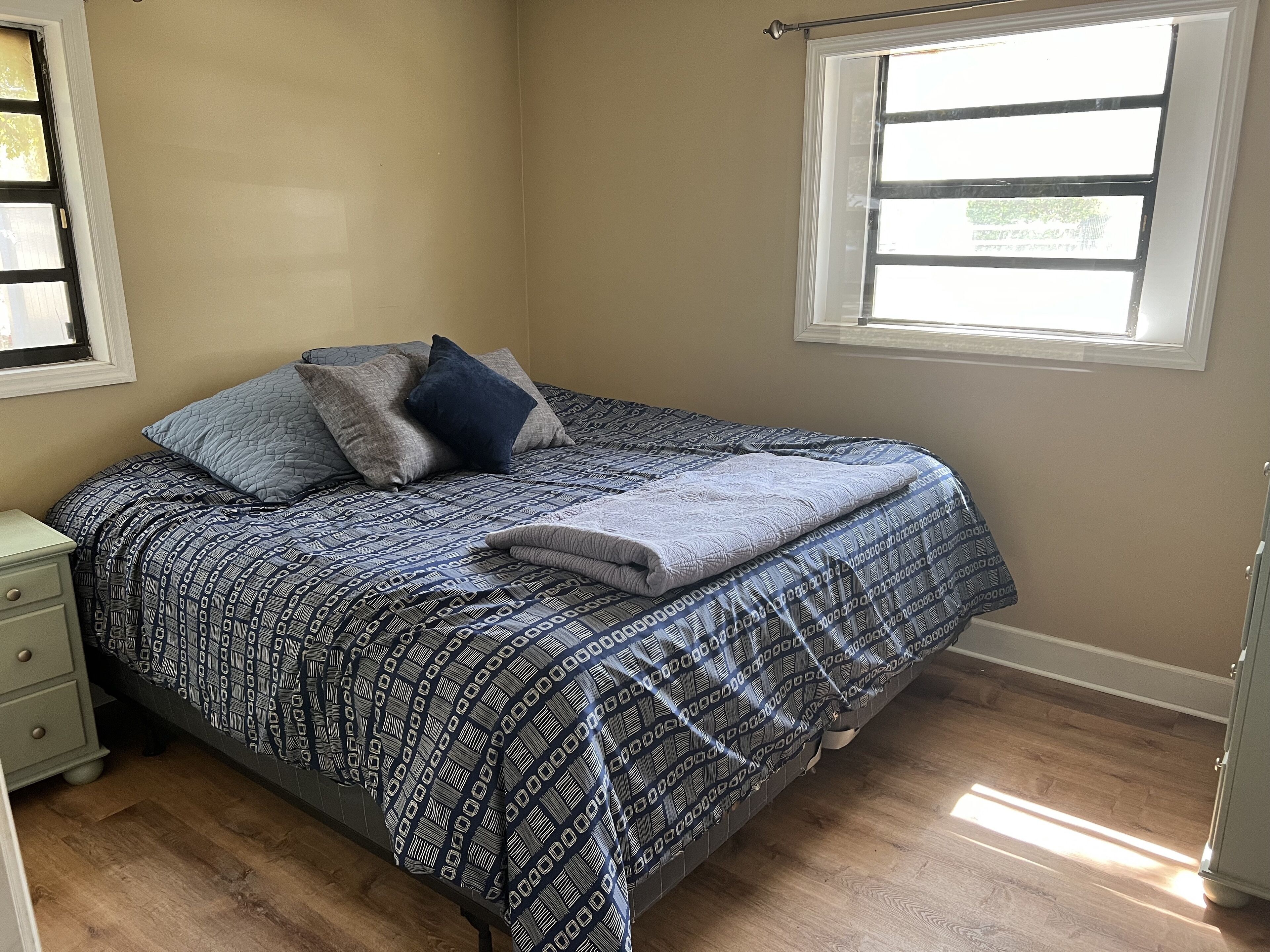 A bedroom with a bed, a nightstand, a window, and a door.