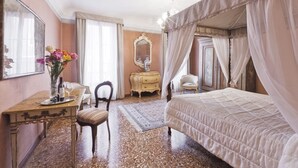 Una camera d'albergo con un letto, una toeletta con uno specchio, una scrivania con una sedia e un vaso di fiori.
