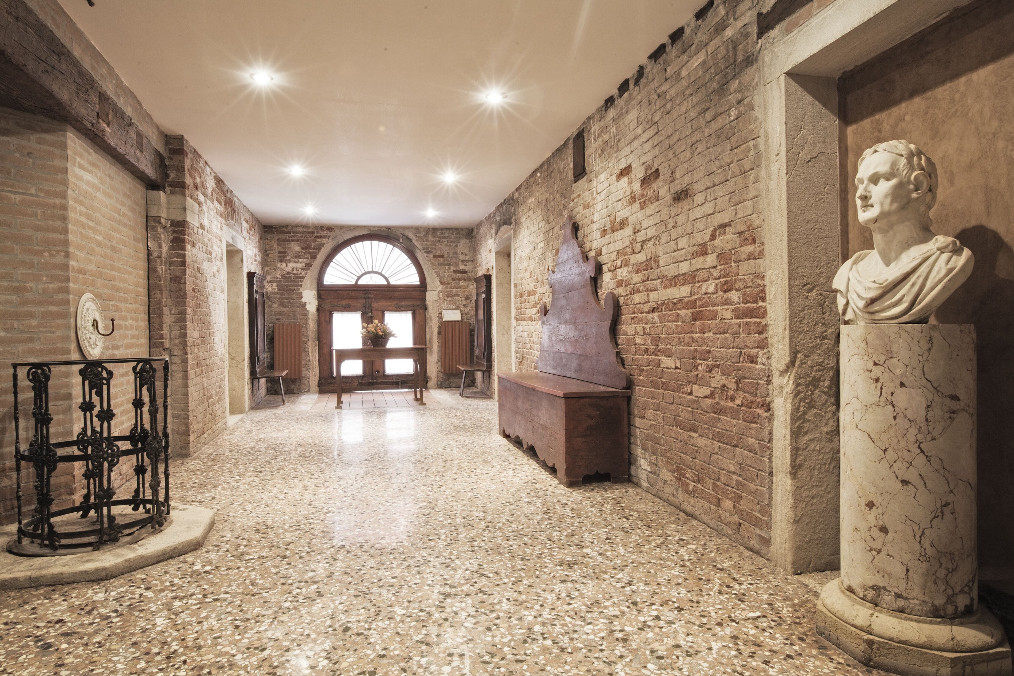 A corridor with brick walls, a marble bust, and a metal sculpture.