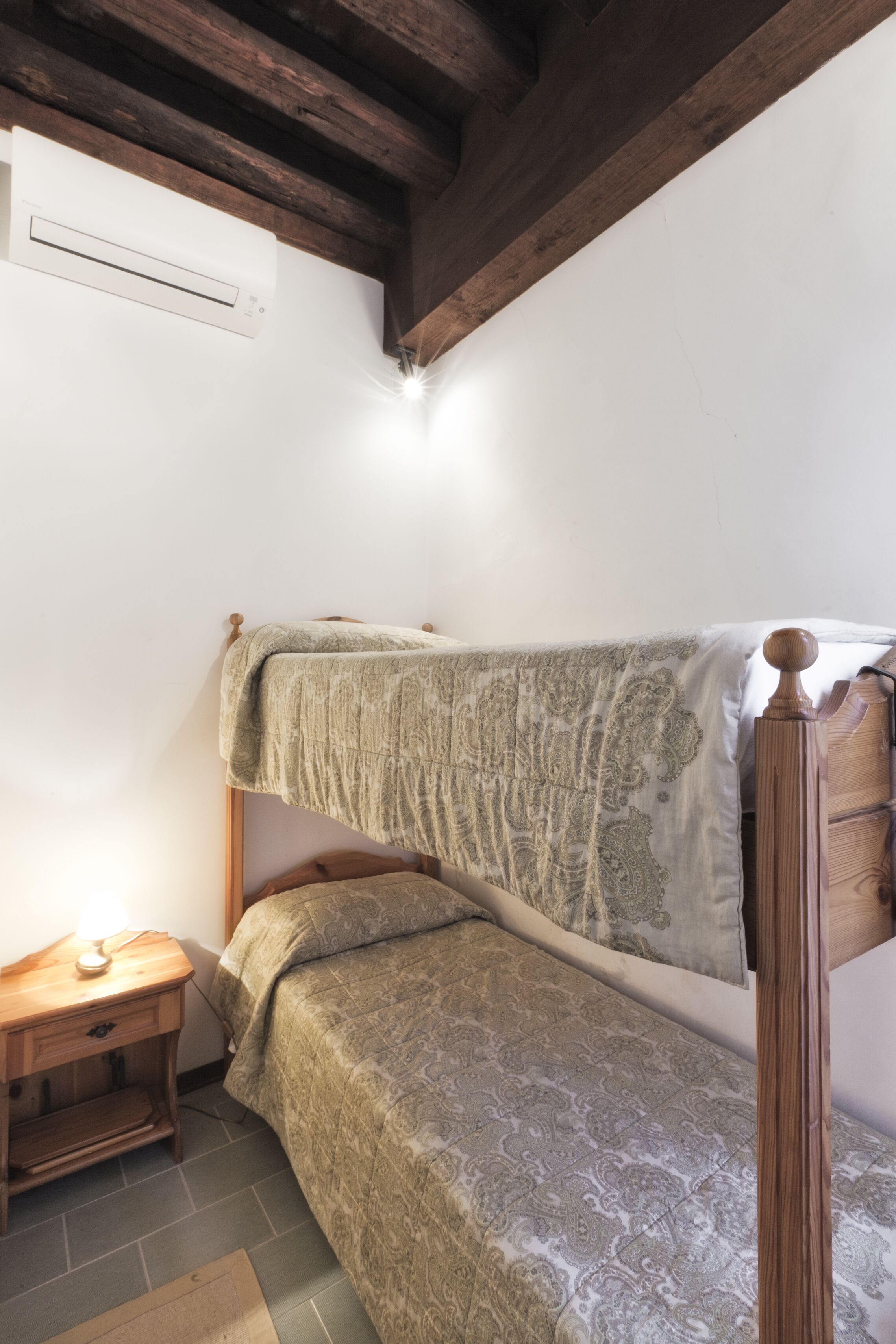 A small, cozy room with a single bed, a nightstand, and a wooden ceiling beam.