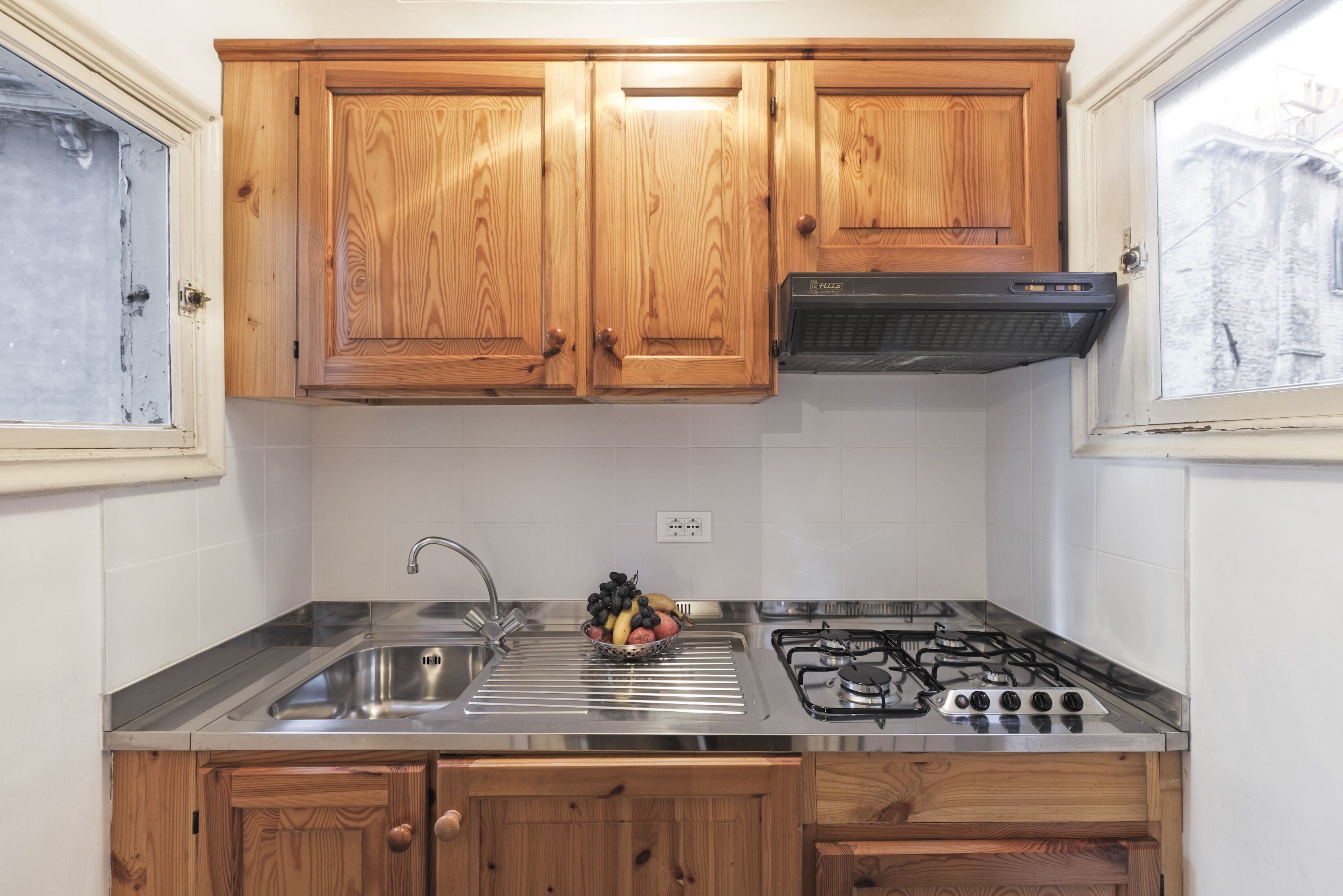 Una cocina con gabinetes de madera, un lavamanos de acero inoxidable, una estufa a gas y un tazón de fruta.