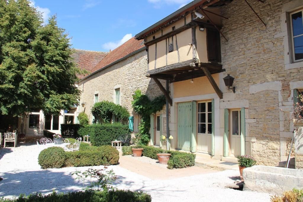 A traditional stone building with a courtyard, featuring a wooden balcony, a door with shutters, and a small table and chair set outside.