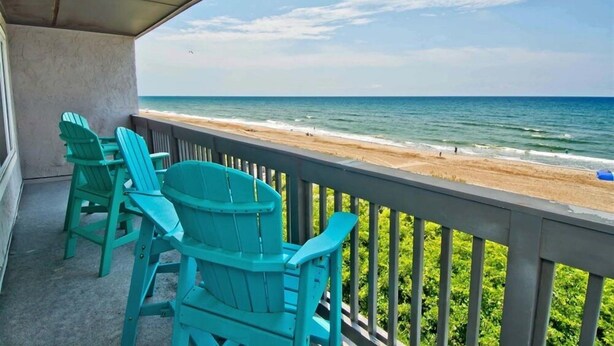 A balcony with turquoise Adirondack chairs overlooking a beach. - Sun Bay 6 - Oceanfront Condo in Atlantic Beach, NC! (Pine Knoll Shores)