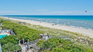 A beach with a wooden walkway leading to a pool area, surrounded by greenery. - Sun Bay 6 - Oceanfront Condo in Atlantic Beach, NC! (Pine Knoll Shores)