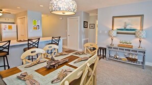 A dining area with a wooden table set for four, a chandelier, and a painting of a ship on the wall. - Sun Bay 6 - Oceanfront Condo in Atlantic Beach, NC! (Pine Knoll Shores)