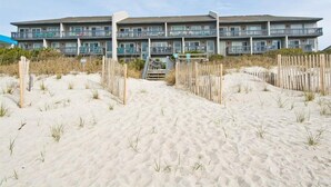 A beachfront hotel with a multi-story structure, a sandy beach in front, and a wooden fence. - Sun Bay 6 - Oceanfront Condo in Atlantic Beach, NC! (Pine Knoll Shores)
