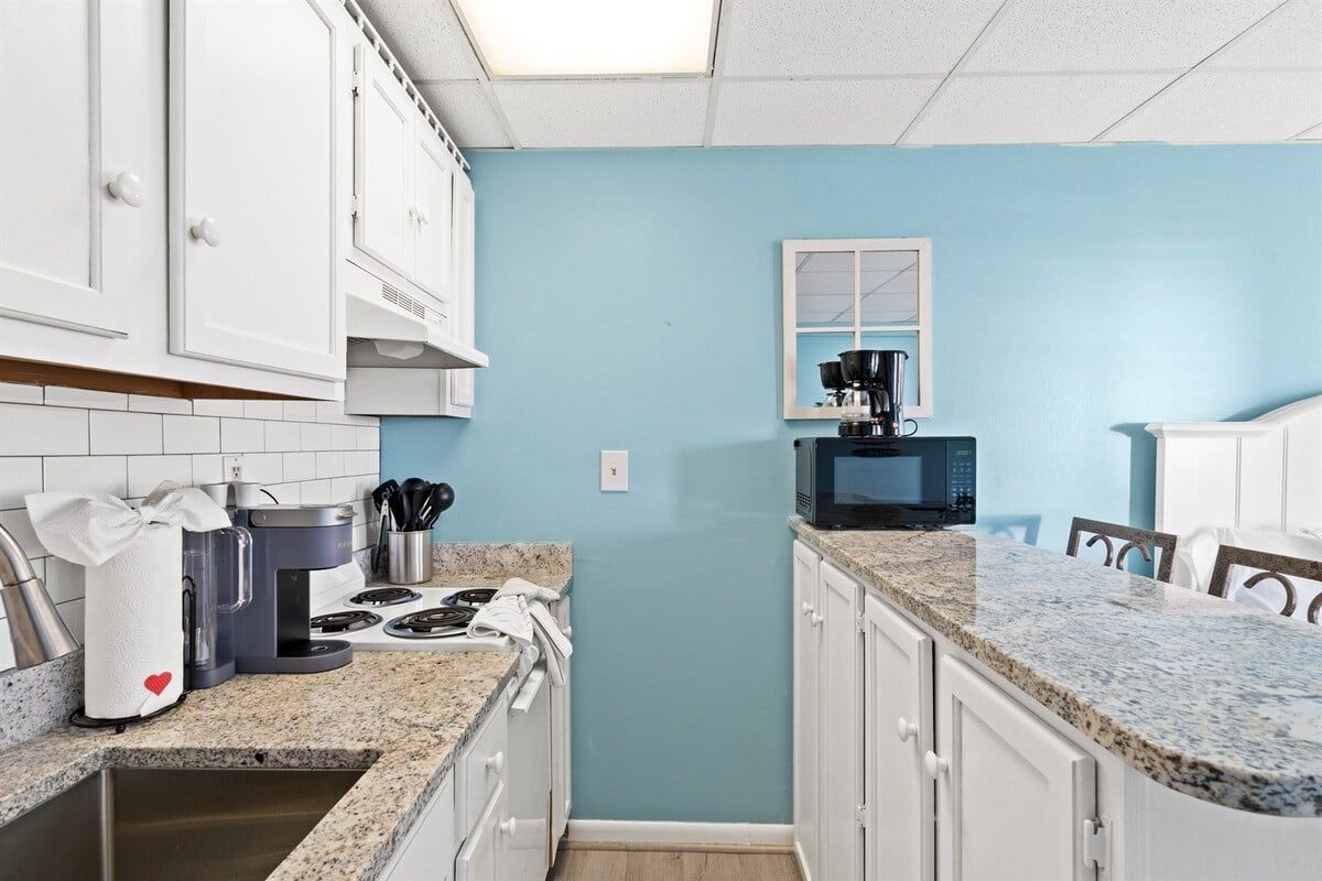 A kitchen with white cabinets, a granite countertop, a coffee maker, and a microwave.