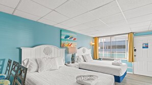 A hotel room with two beds, a painting of beach umbrellas, a lamp, and a door with a sign. - Beachfront Studio, Sleeps 3, Pool (Panama City Beach)