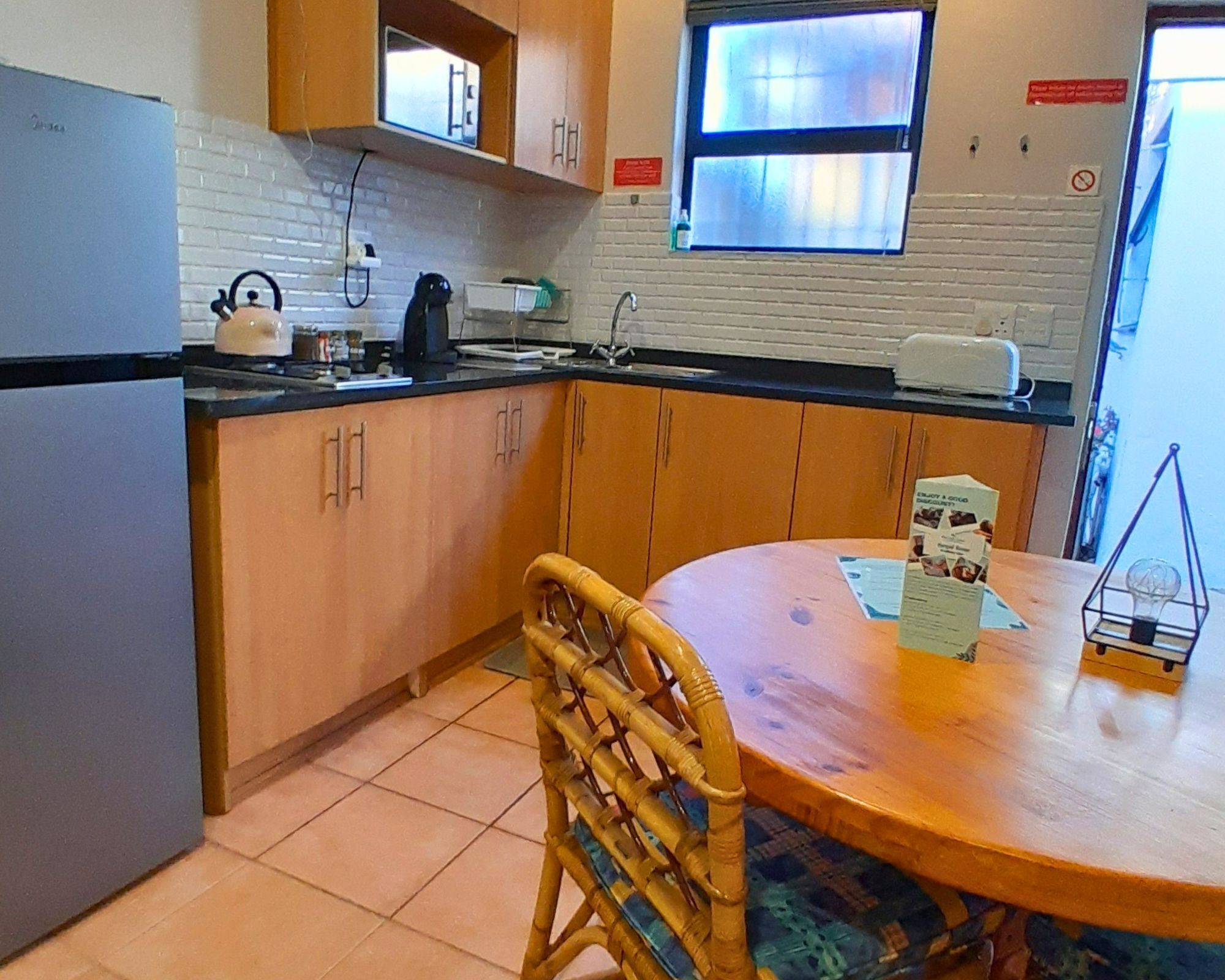 A kitchen with wooden cabinets, a refrigerator, a kettle, and a table with a menu.