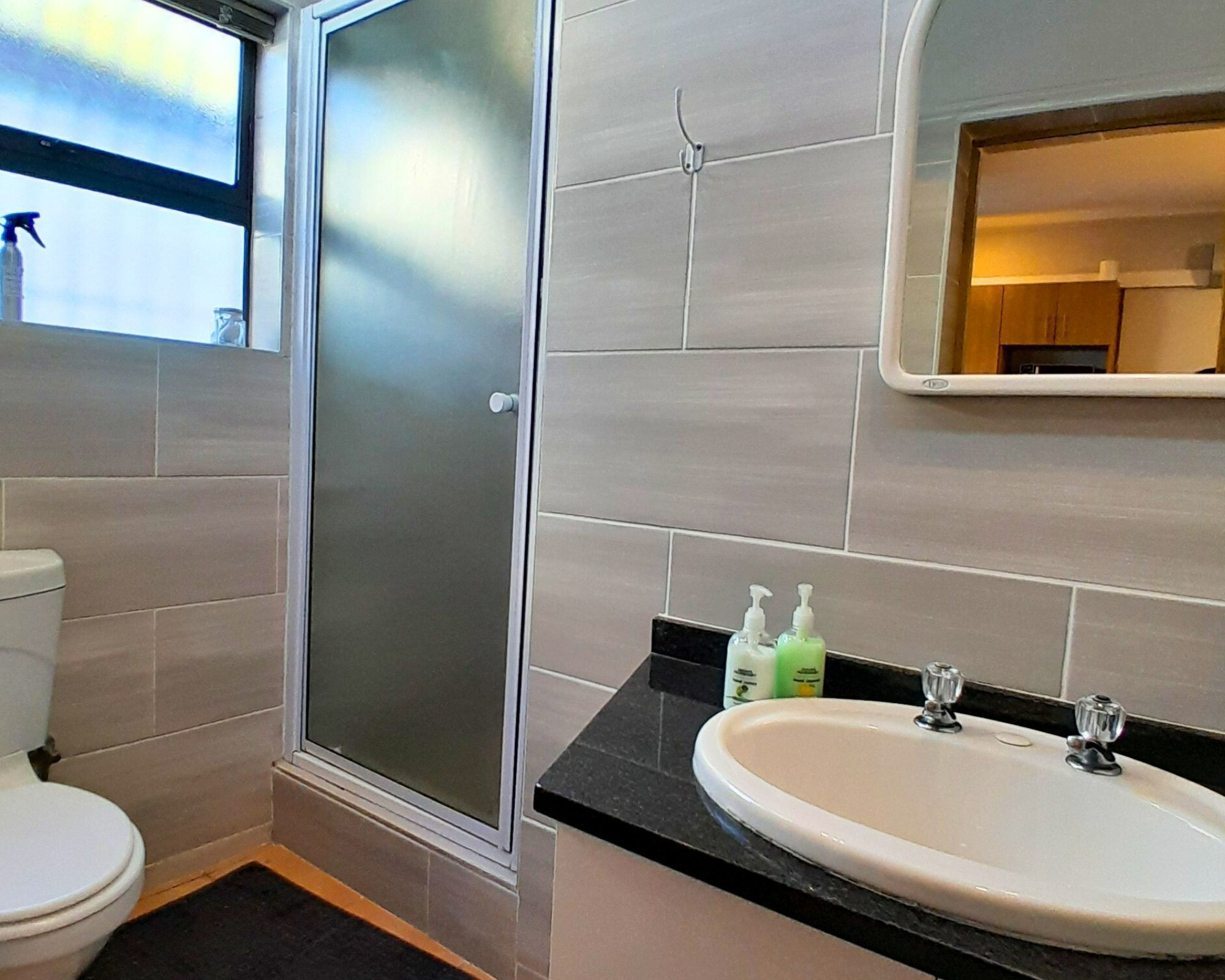 A bathroom with a toilet, a shower with frosted glass doors, a sink with a mirror above it, and toiletries on the countertop.